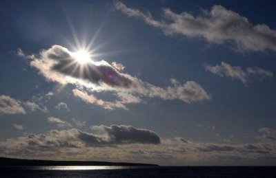 sun peeking through the clouds over water