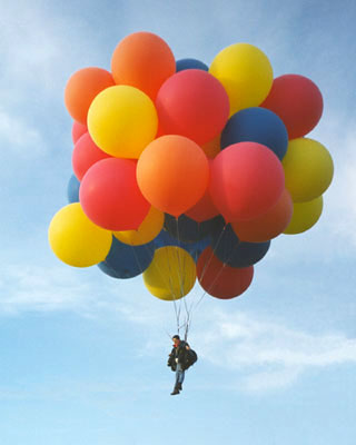 A guy hanging from some helium balloons