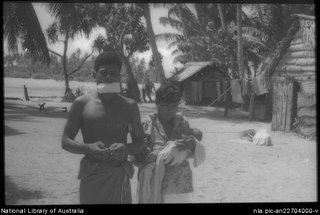 Man and woman holding a baby with house in background on the Carteret Islands, Papua New Guinea, 1960. Photo by Terence and Margaret Spencer. From the National Library of Australia.