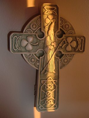 celtic cross with St. Patrick on it being hit by thin vertical stripe of early morning sunlight