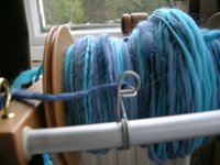 close up view of singles yarn on bobbin,  various shades including turquoise and grey