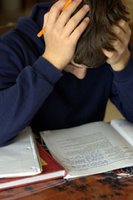 Teen boy at desk, poring over books and papers: head in hands