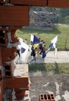 People carrying Bosnian flags pass by destroyed houses during the second day of a four-day march to Srebrenica, in the village of Liplje near Zvornik, 120 km (75 miles) north of Sarajevo, Saturday, July 8, 2006. Hundreds of Bosniaks began a four-day march on Friday along the route survivors used 11 years ago to escape the Bosnian Serb killings in Srebrenica, the worst massacre in Europe since World War II. (AP Photo/Amel Emric)