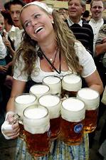 Photo of pretty buxom beer wench holding 8 beers and smiling.
