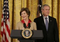 President George W. Bush listens on as Mrs. Laura Bush welcomes women leaders to the East Room for a celebration Tuesday, March 7, 2006, of International Women's Day. Mrs. Bush said, 'I've been privileged to meet thousands of women from many nations, and I believe that women everywhere share the same dreams -- to be educated, to in peace, to enjoy good health, to be prosperous, and to be heard.' White House photo by Kimberlee Hewitt.