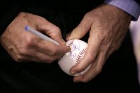 After warming up with a few pitches, President George W. Bush signs a baseball shortly before throwing one over the plate for the opening game between the Cincinnati Reds and the Chicago Cubs in Cincinnati, Ohio, Monday, April 3, 2006. White House photo by Eric Draper.