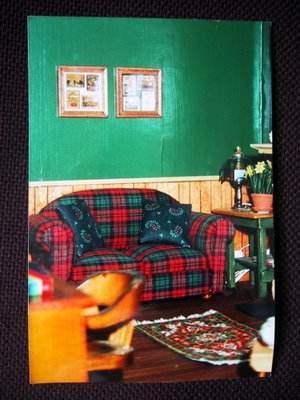Dolls' house miniature study, with green painted walls with wainscoating, and a green and red plaid sofa.