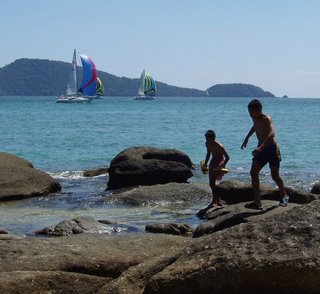 A couple of local lads run across the rocks as the boats sail past Laem Ka Beach
