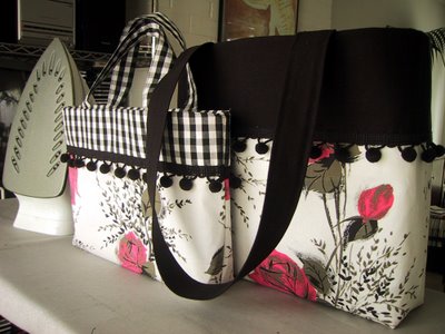 Two hand-made bags in colours of pink, white and black, displayed on an ironing board with an iron.