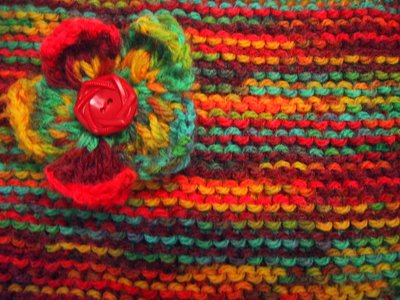 Multi-coloured garter stitch knitting, with a knitted flower made from the same wool with a button in the centre, pinned to it.