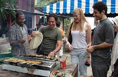 MALAYSIAN DELICACY: Ratigan trying his hand at grilling satay. With him are Dr Zambry (left), Mason and Iranian tourist Reza Khedmati.