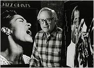 William P. Gottlieb in 1992, between two of his best-known photographs: portraits of Billie Holiday and Louis Armstrong.