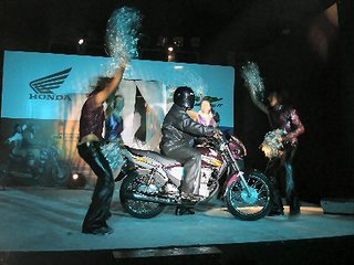 The girls hide behind the bike, much to the audiences display. Rider plays L-O-N-D-O-N statue