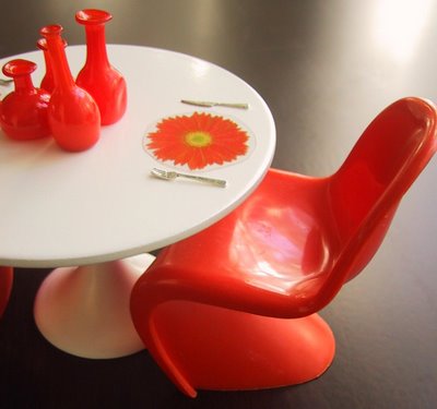 Modern dolls' house miniature Saarinen table with orange Panton chair, glass bottles and flower-shaped place mats.