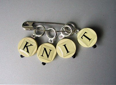 Four completed knitting stitch markers, with the letters K, N, I and T on them.